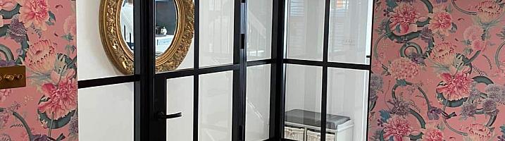 Internal black steel-look corner screen and door in a dining room with pink floral wallpaper and green velvet chairs