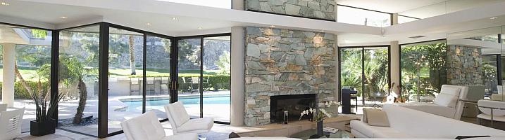 Modern living room with a stone fireplace, white sofas, and large black sliding doors open to a pool
