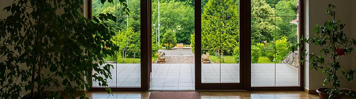 Brown glass-panelled French doors open to a sunny, green landscape, viewed from a tiled hallway