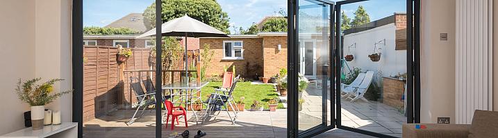 Dark grey Origin OB-49 bifold doors partially open, viewed from a living room, looking out onto a sunny garden deck