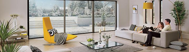 Couple relaxing on a sofa in a modern living room with large Origin sliding doors looking out onto a snowy garden