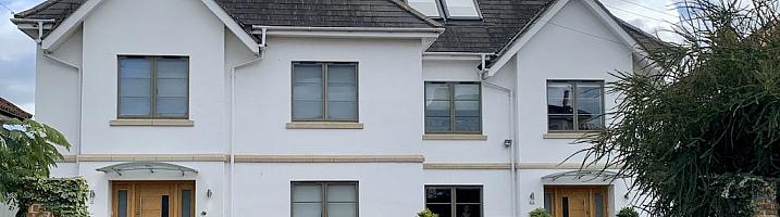 Large white house with two wooden front doors, featuring numerous grey-green aluminium casement windows