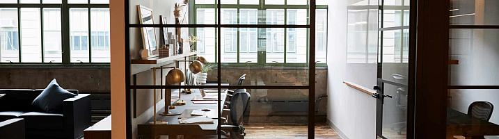 A modern office with a black steel-look glass screen and a matching door, separating a hallway from a desk area