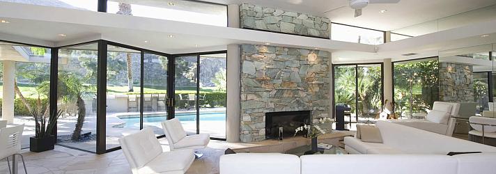 Modern living room with a stone fireplace, white sofas, and large black sliding doors open to a pool