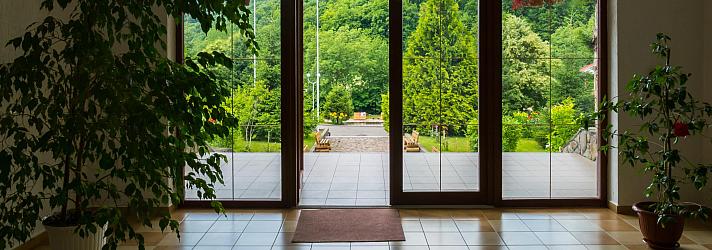 Brown glass-panelled French doors open to a sunny, green landscape, viewed from a tiled hallway