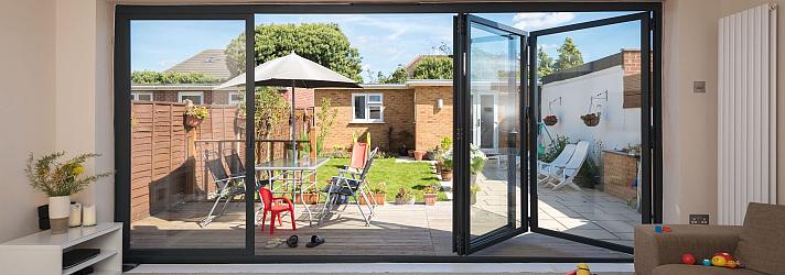 Dark grey Origin OB-49 bifold doors partially open, viewed from a living room, looking out onto a sunny garden deck