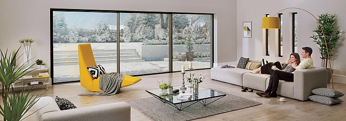 Couple relaxing on a sofa in a modern living room with large Origin sliding doors looking out onto a snowy garden