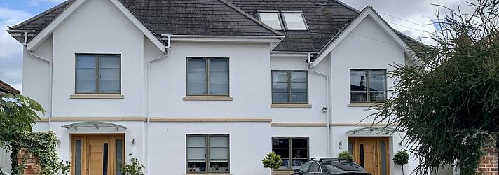 Large white house with two wooden front doors, featuring numerous grey-green aluminium casement windows