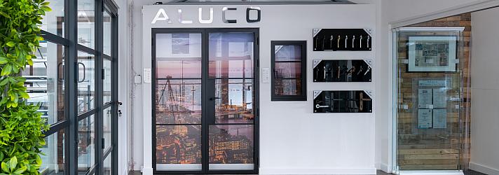 Wide view of the Aluco showroom display wall, featuring steel-look doors, a window, handle options, and a green wall
