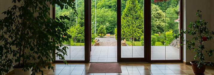 Brown glass-panelled French doors open to a sunny, green landscape, viewed from a tiled hallway