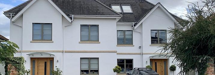 Large white house with two wooden front doors, featuring numerous grey-green aluminium casement windows