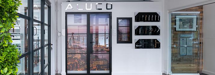 Wide view of the Aluco showroom display wall, featuring steel-look doors, a window, handle options, and a green wall