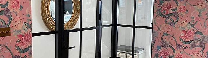 Internal black steel-look corner screen and door in a dining room with pink floral wallpaper and green velvet chairs