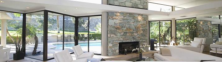 Modern living room with a stone fireplace, white sofas, and large black sliding doors open to a pool