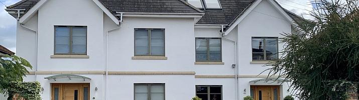 Large white house with two wooden front doors, featuring numerous grey-green aluminium casement windows