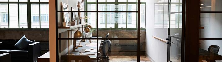 A modern office with a black steel-look glass screen and a matching door, separating a hallway from a desk area