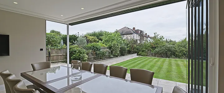 Dining room with bifold doors fully open, showing a wide view of a long, manicured lawn and garden