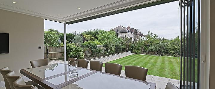 Dining room with bifold doors fully open, showing a wide view of a long, manicured lawn and garden