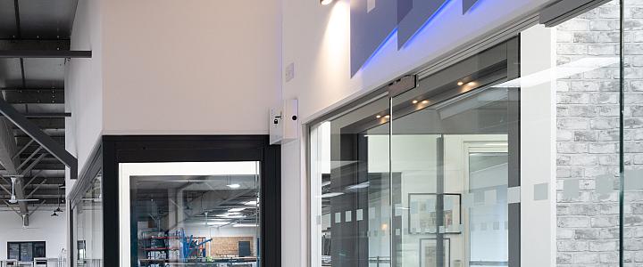A modern office hallway with a blue backlit 'FGC' logo above frameless glass doors and a black-framed door