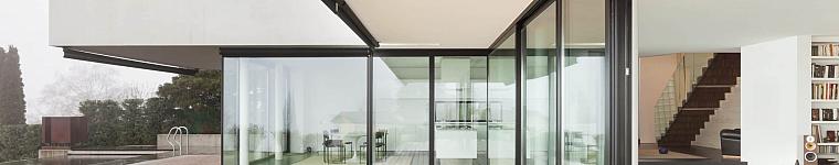 Modern white house with a wooden deck, black-framed sliding glass doors, and a seamless indoor-outdoor living space