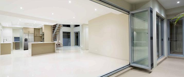 Silver aluminum bifold doors fully folded open, revealing a large, modern, empty room with a kitchen and tiled floors