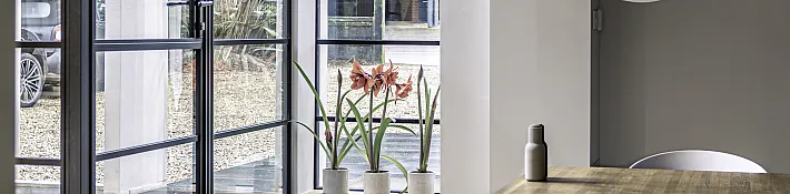 Modern dining area with steps leading up to a black steel-look door and window, showing amaryllis flowers on the sill
