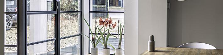 Modern dining area with steps leading up to a black steel-look door and window, showing amaryllis flowers on the sill