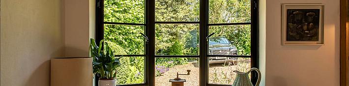 black, three-panel steel-replacement window with traditional handles, looking out onto a garden and driveway