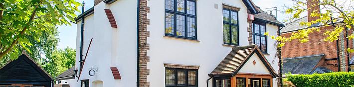 A white house with brick quoins, featuring black aluminium windows with a traditional leaded-style grid.