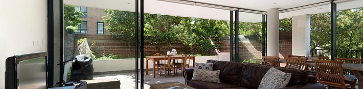 Bright living room with a brown leather sofa and large black sliding doors open to a sunny patio with a dining table