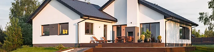 The back of a modern white house at sunset, showing a large wooden deck and several dark-framed aluminium windows