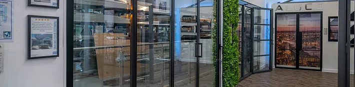 A showroom with herringbone floors and a large black bifolding door, with a green wall and another door in the back