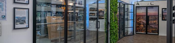 A showroom with herringbone floors and a large black bifolding door, with a green wall and another door in the back