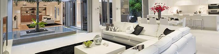 "Luxurious living room with white sofas and Origin OB-72 bifold doors open to an internal courtyard with a palm tree