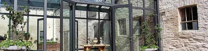 Exterior of a grey Alitherm glass conservatory with an open double door, set against a rustic stone building