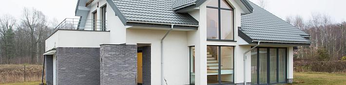 A modern white house with large, dark-framed aluminium windows, including a tall corner window and sliding patio doors