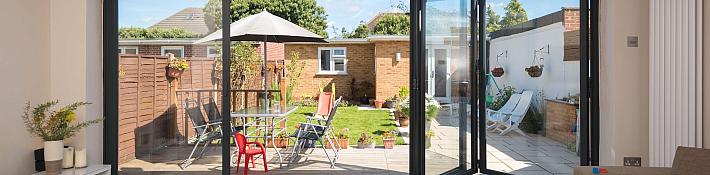 Dark grey Origin OB-49 bifold doors partially open, viewed from a living room, looking out onto a sunny garden deck