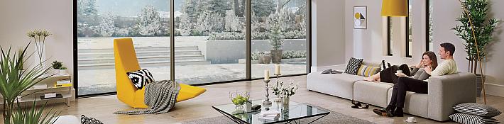 Couple relaxing on a sofa in a modern living room with large Origin sliding doors looking out onto a snowy garden