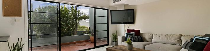 A living room with a sofa and a black steel-replacement sliding door with horizontal bars, leading to a balcon
