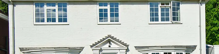 A white brick house with three white aluminium windows on the top floor, featuring a grid pattern. One window is open.