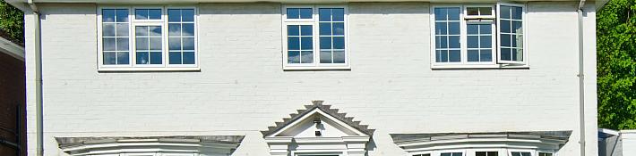 A white brick house with three white aluminium windows on the top floor, featuring a grid pattern. One window is open.