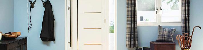 Modern white Origin front door with horizontal strips and a long handle, viewed from inside a light blue entrance hall