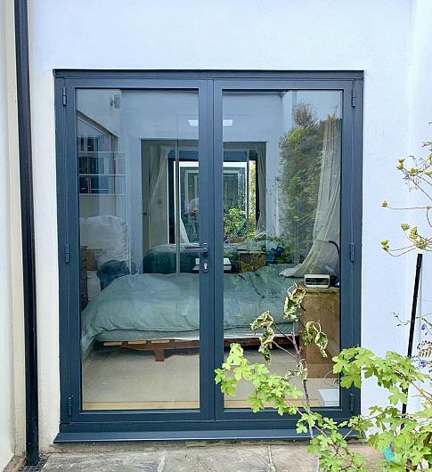 Closed, dark grey two-panel Origin OB-49 bifold doors, viewed from outside, looking into a modern bedroom