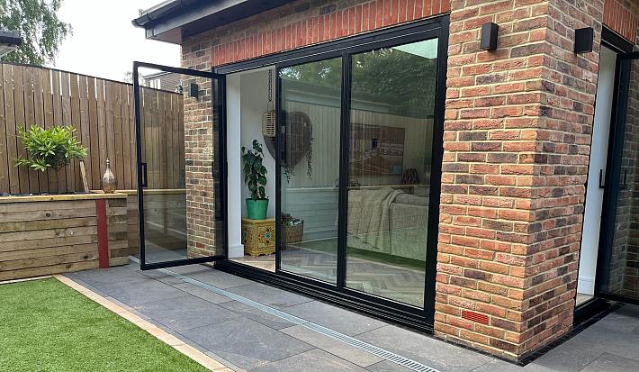 Exterior of a brick extension with black slimline sliding doors. A single traffic door is open to the patio