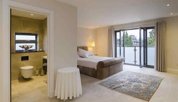Modern bedroom with dark grey aluminium doors open to a balcony, and a view into the en-suite bathroom