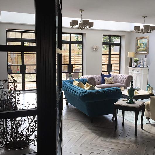 Elegant living room with velvet sofas and a large, black Aluco steel-look door and window system looking onto a patio
