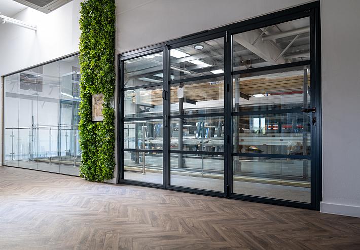 Large black Aluco steel-look bifold or sliding door with horizontal bars, installed in the showroom next to a green wall