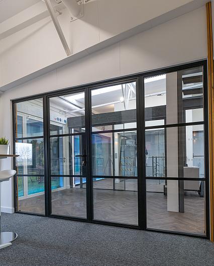 A large, black steel-replacement internal screen and door set with a grid pattern, installed in a modern showroom.