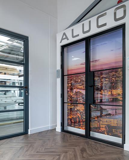 Close-up of the Aluco showroom display, showing a black steel-look double door with a city graphic and another grey door