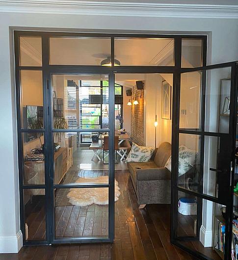 Black steel-look double doors with side and top panels, shown open and leading from a hallway into a living room